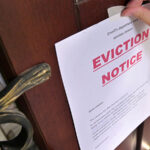 A woman tapes an “Eviction Notice” onto the front door of her tenant’s apartment.