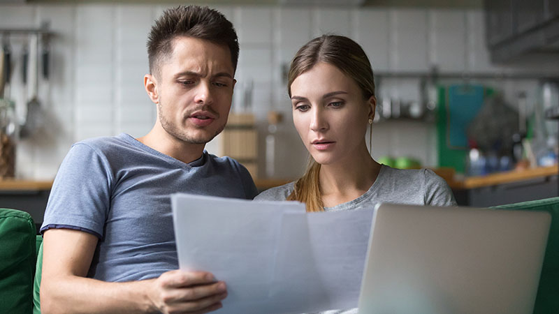 Bad-credit-while-renting-1 A man and a woman sit on the couch together as the couple tries to figure out their bad credit score.