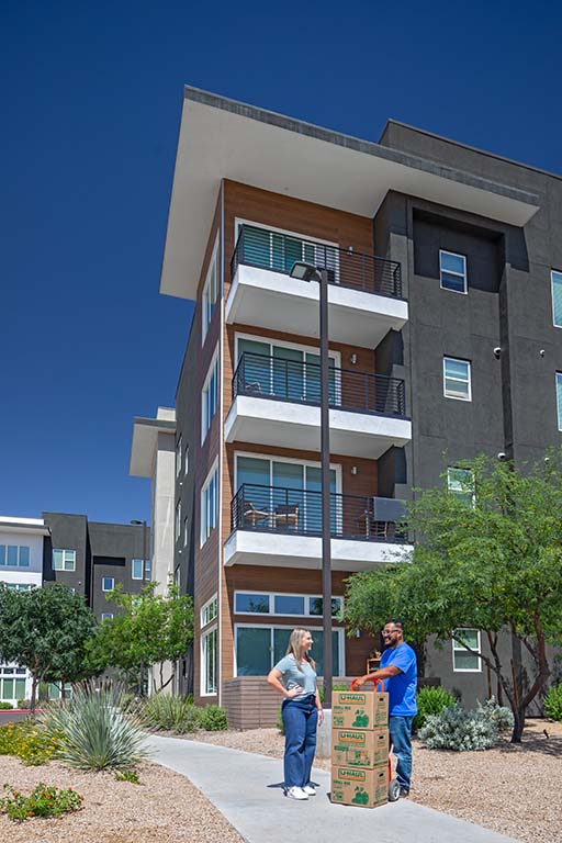 A female customer stands next to a male Service Provider while they discuss her move. A dolly with moving boxes rests between them.