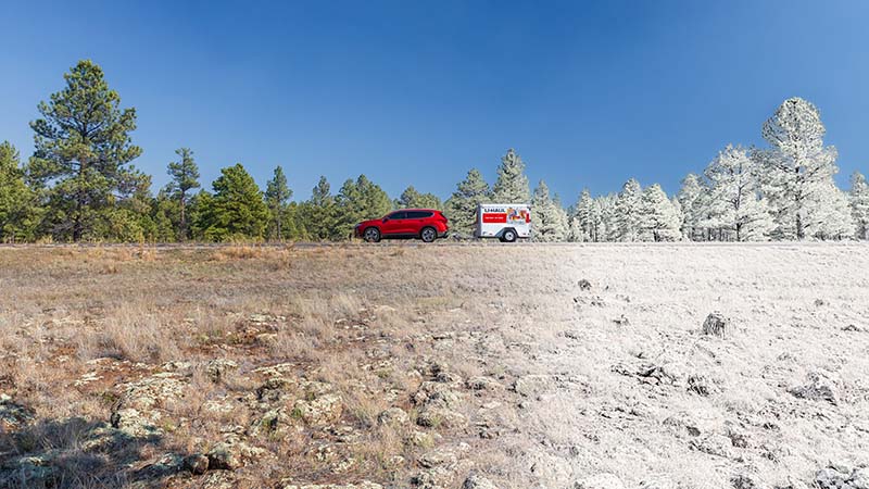 Moving-during-holidays-1 An SUV is driving on a highway during the winter. It’s pulling a U-Haul cargo trailer.