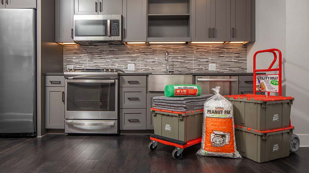 Rent-after-eviction-1 An empty kitchen apartment can be seen. Multiple U-Haul Ready-To-Go Boxes, packing peanuts, furniture blankets, Enviro-Bubble®, and a dolly sit together in the kitchen.