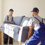 Two Service Providers work together to carefully move a couch. Customers can use job relocation assistance to help them move for a new position.