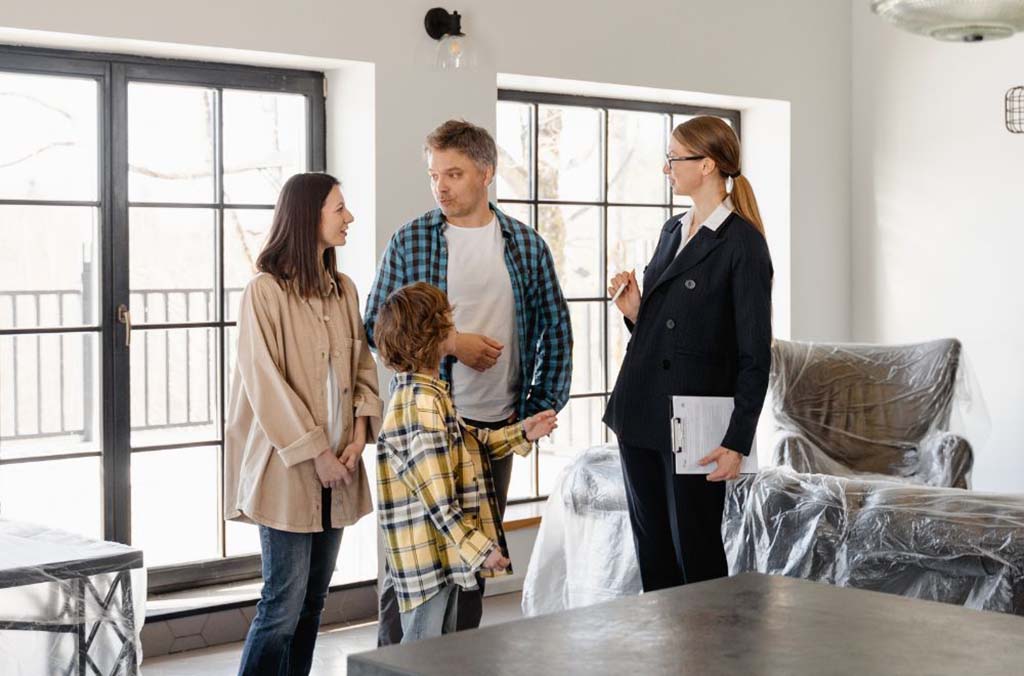 A real estate agent talks to the husband, wife, and a child inside a house.