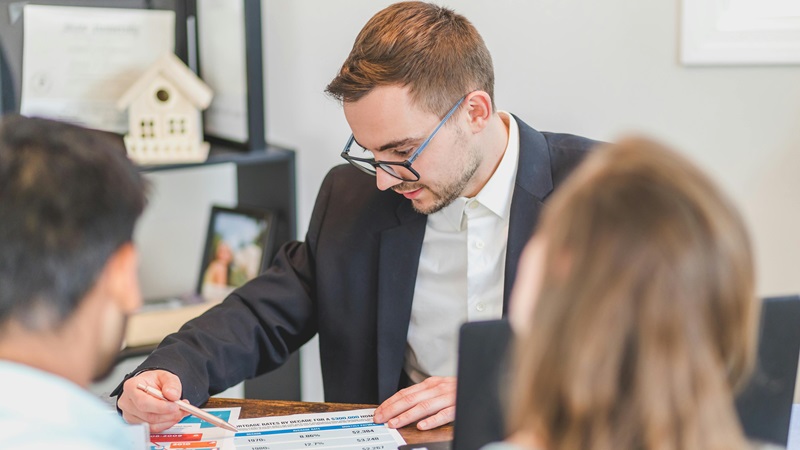 A man points to his document with a pencil to the husband-and-wife couple.