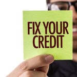 A man wearing glasses holds a sticky note that reads: “Fix Your Credit.”