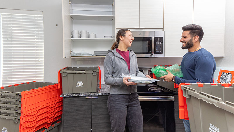 A husband and wife pack their kitchen items into U-Haul Ready-to-Go® Boxes as they prepare to move from their apartment to their new home as first-time homebuyers.