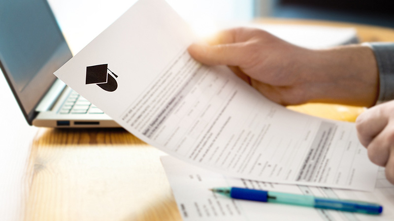 A person reviews a document from a student loan letter with a computer sitting in the background on a table.