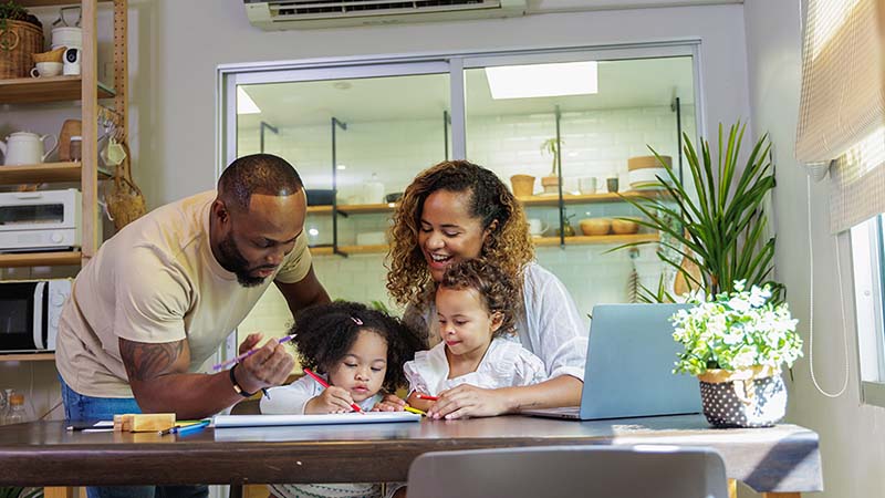 A husband and wife work together to help their two children with their activity on the dining room table.
