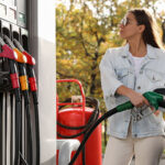A woman fills her car with gasoline at a gas station. Gas prices in 2026 are much higher than expected when experts made their predictions at the beginning of the year.