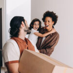 A Canadian family consisting of a mother, father, and a young child, smile together as they move into their new home.