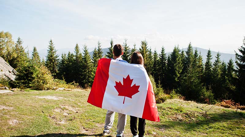 Two young children stand side-by-side with a Canadian flag draped over their shoulders.