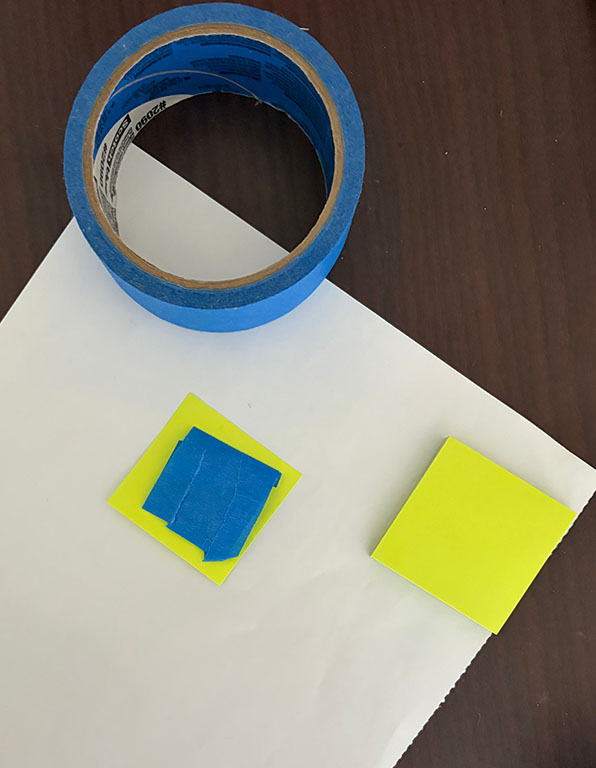 A sticky note with painter’s tape on it is on the back side of a poster. Dorm decorating tips can help add character to your space.