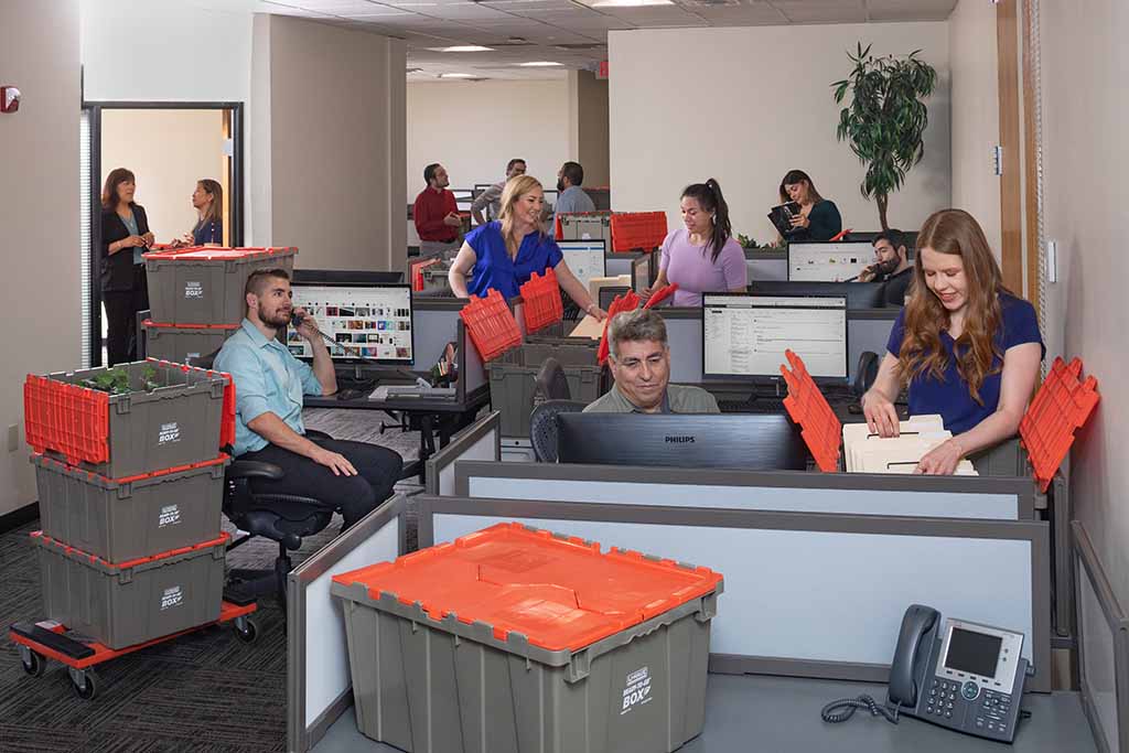 An office full of employees is packing items into U-Haul Ready-To-Go Boxes®. Job relocation packages make moving for work easier and ensure a smooth transition.