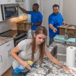 A woman wipes the kitchen counters in her apartment while two male Service Providers unpack boxes. What is a long-term lease, and what are the positives and negatives of signing one?