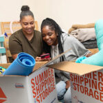 Two women are looking on a phone in their college dorm. They moved into college as out-of-state students.