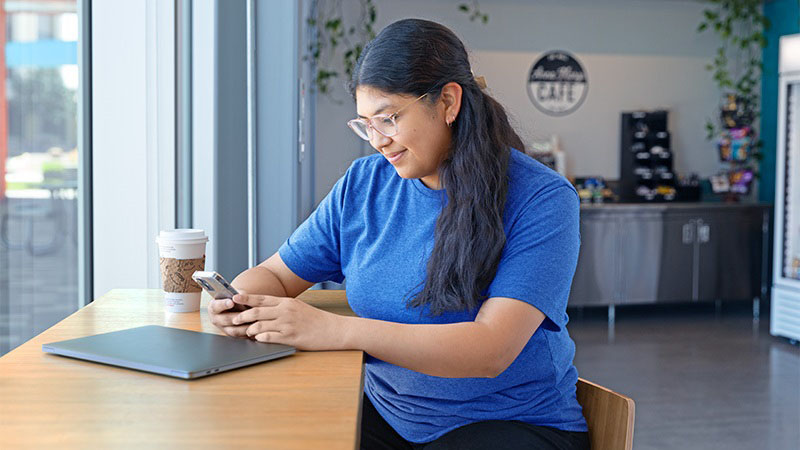 A young woman is viewing homes for sale in her area on her phone while sitting in a cafe.