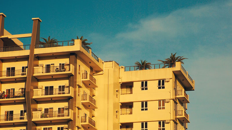 The top of a condo building is seen at sunset. Palm trees sit on the condo's rooftop.