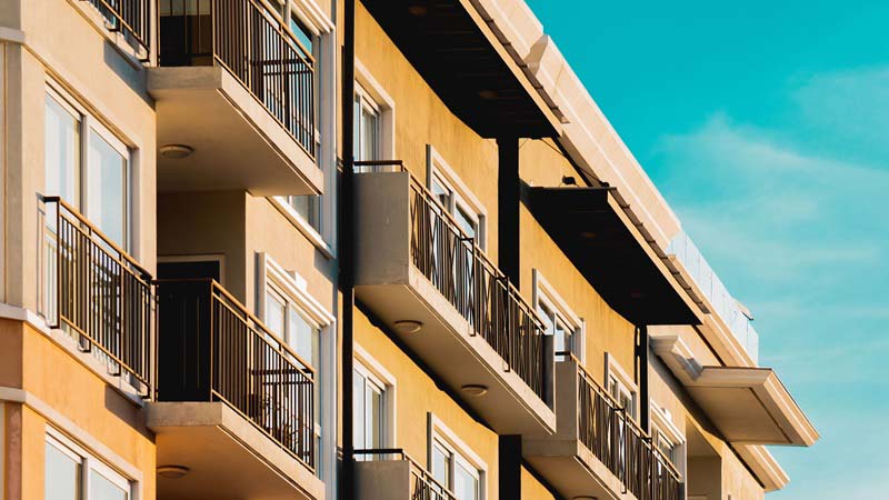 The side of an apartment building is seen on a sunny afternoon. Each apartment has a small balcony.