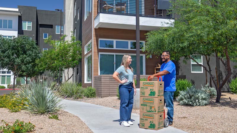 A Moving Helper talks to a young woman outside her apartment building while he moves her belongings.