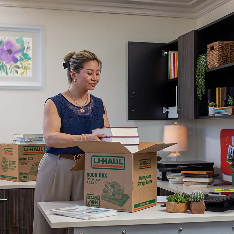A woman packs books into a box in her office. Job relocation offers many moving benefits.