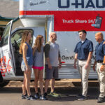 Three Moving Helpers talk to a family next to a U-Haul truck rental parked next to a house. The three helpers unloaded the family’s belongings into their new home.
