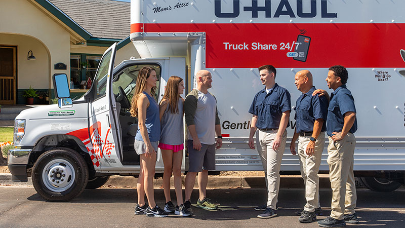 Submit-a-review-1 Three Moving Helpers talk to a family next to a U-Haul truck rental parked next to a house. The three helpers unloaded the family’s belongings into their new home.