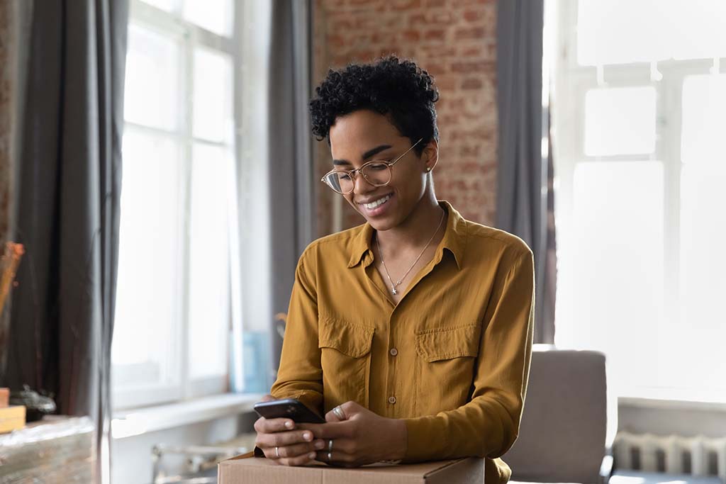A woman smiles down at her phone as she leaves a positive review for her Moving Help Service Provider.