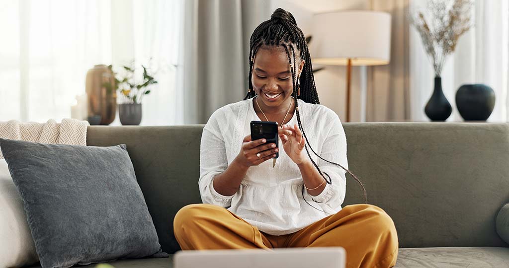 A woman sits on the couch while she fills out a Moving Help review on her phone.