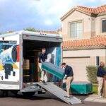 A Service Provider shakes hands with a couple while two Moving Helpers carefully unload a piece of furniture out of a U-Haul truck rental.