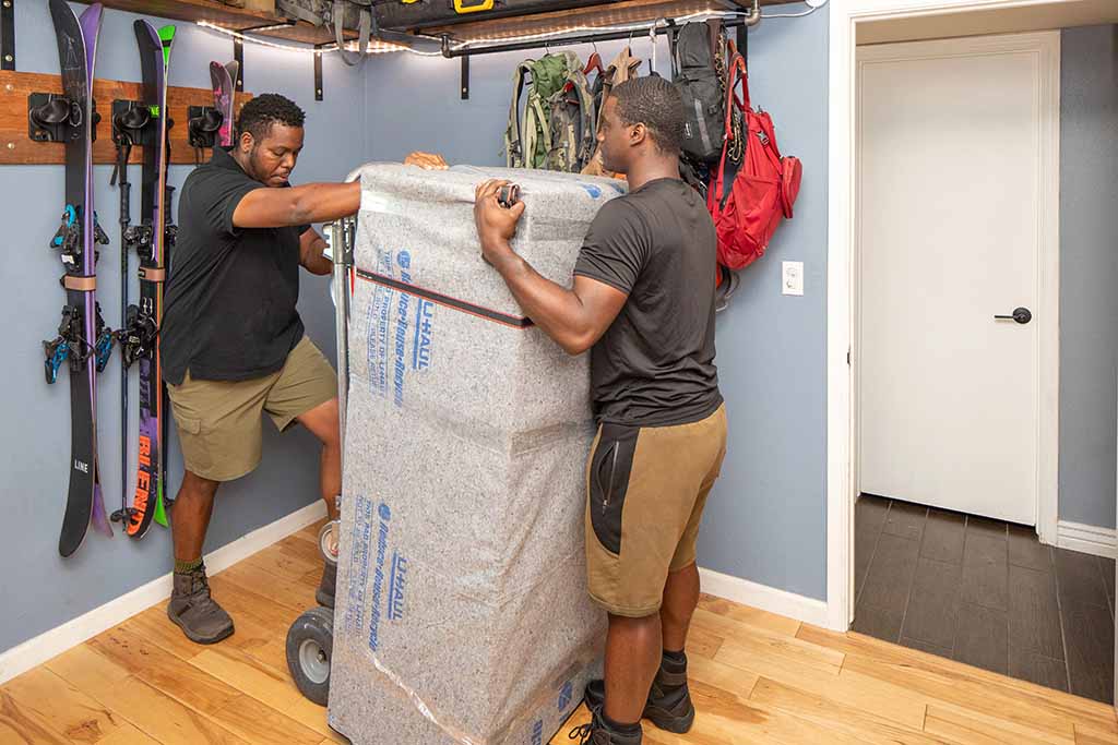 Two Moving Helpers work together to begin moving a protected gun safe onto a dolly.