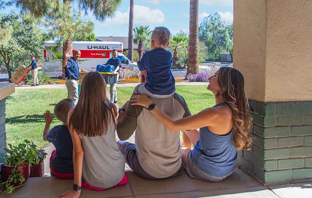 A family sits on a front porch together as the Service Providers load their belongings into a U-Haul truck rental.